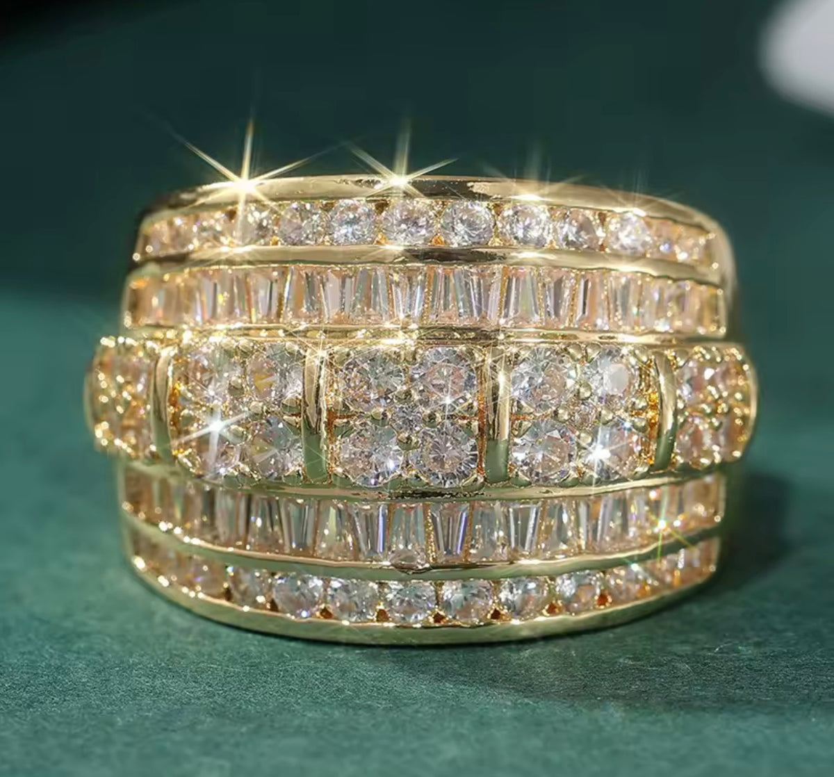 A gold multi-row diamond eternity ring with baguette and round-cut stones, set against a dark green textured background.