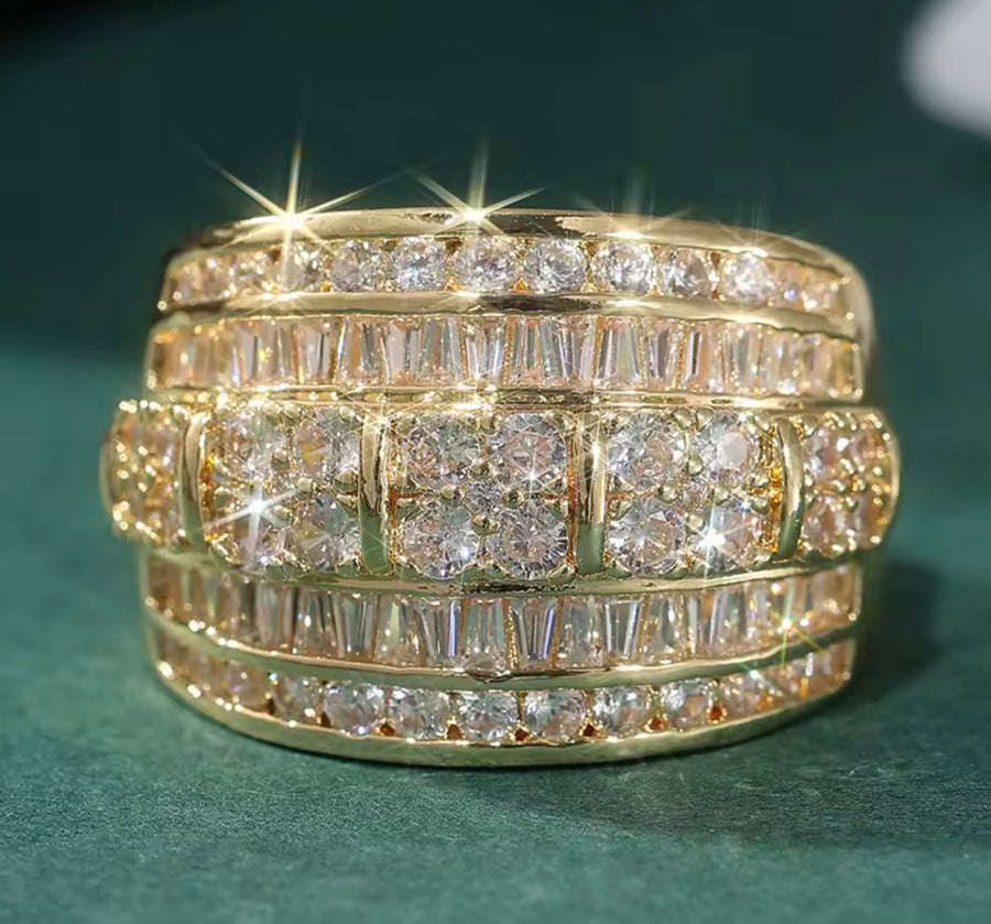 A gold multi-row diamond eternity ring with baguette and round-cut stones, set against a dark green textured background.