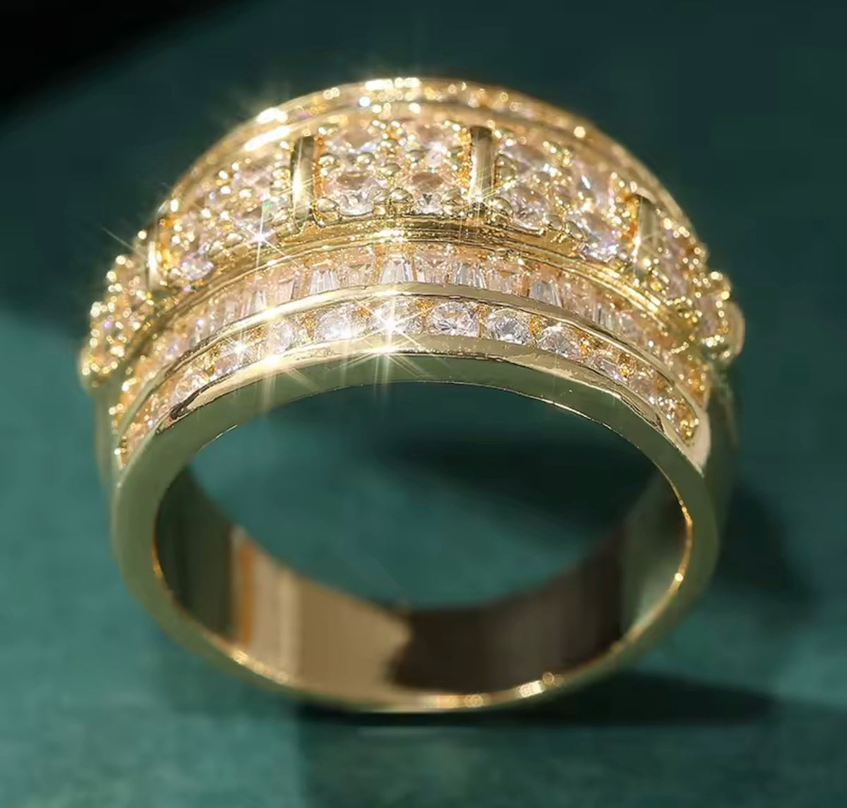 A gold ring with multiple rows of clear gemstones, photographed close-up on a dark green background.